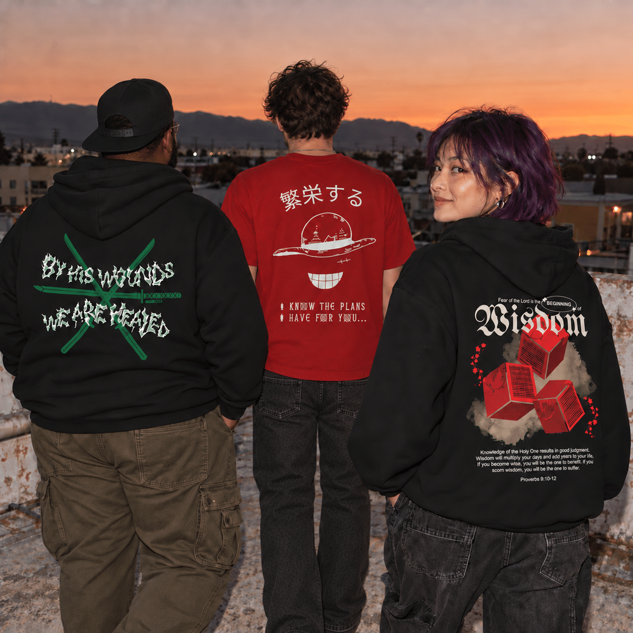 Three friends on a rooftop at sunset wearing DTruest Threads: the By His Wounds hoodie, the I Know the Plans tee and the Beginning of Wisdom hoodie