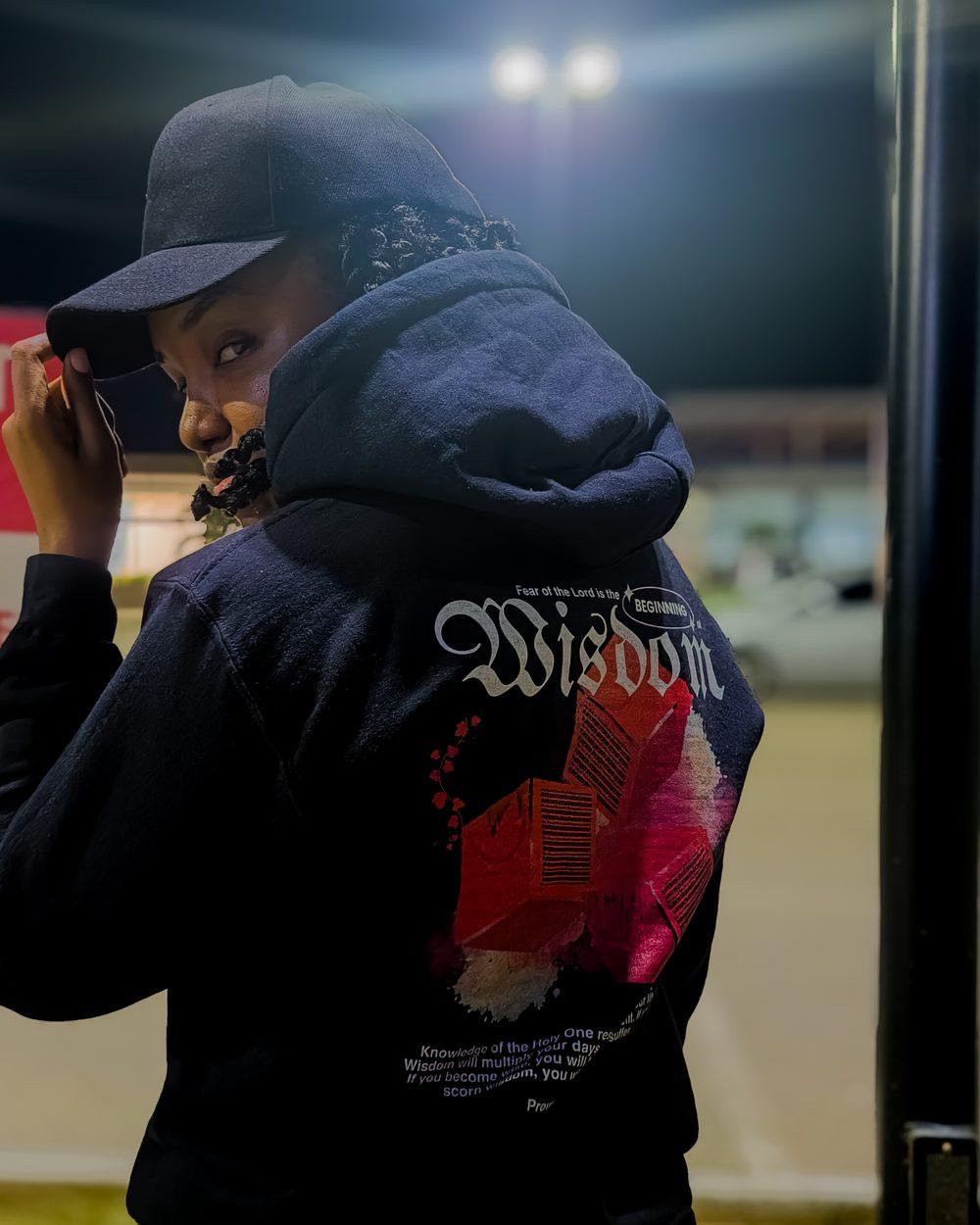 Tiffany in a cap looking back over her shoulder at night, wearing the Beginning of Wisdom hoodie